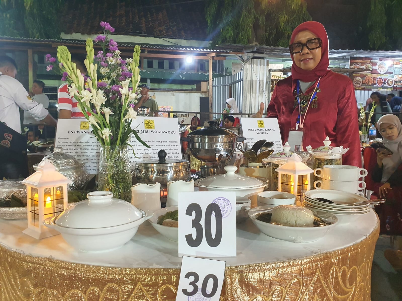 JUARA. Aisyah, Owner Resto Osyfood, berpose di depan meja sajian kuliner saat Madura Culinary Festival 2025 di Taman Bunga Sumenep. (dok.Redaksi Linkking.id)